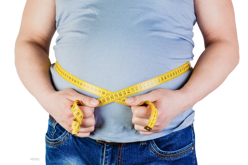 Overweight man holding a measuring tape around his midsection