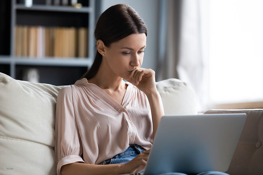 Young brunette woman sitting on couch looking pensively  at her laptop